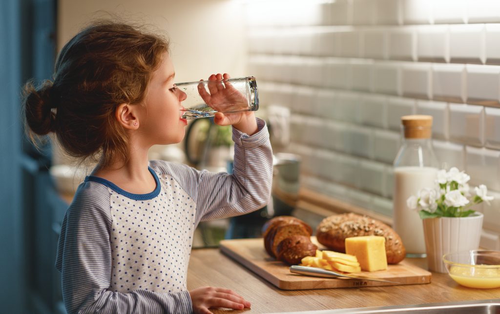 Young girl drinking alkaline filtered water in kitchen